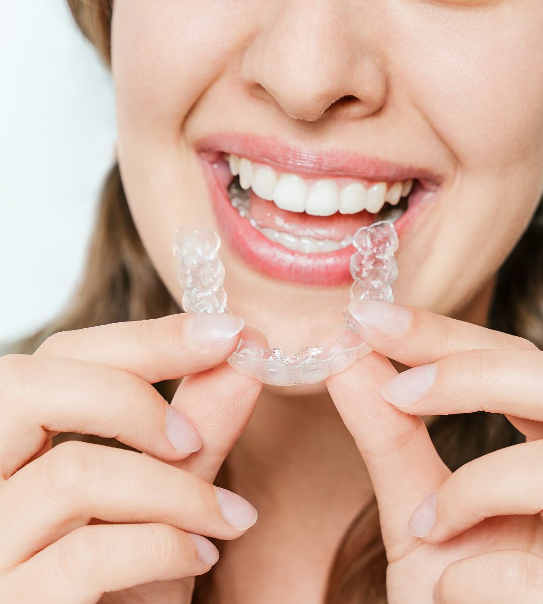 Primer plano de una mujer adulta en Rivas sonriendo ampliamente y sosteniendo un alineador transparente de ortodoncia invisible con ambas manos frente a su boca, mostrando su discreción y estética.